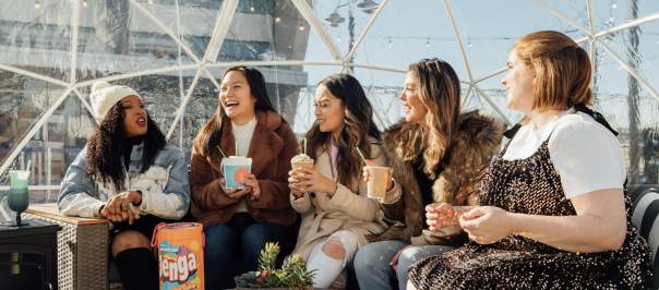 Image is of 5 women sitting in a clear igloo, laughing and having fun.