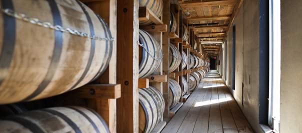Rows of bourbon barrels line the left side of the photo in a wooden rickhouse.