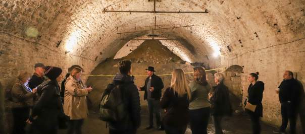 A group of people gather to listen to a tour guide in one of Cincinnati's underground lagering tunnels.