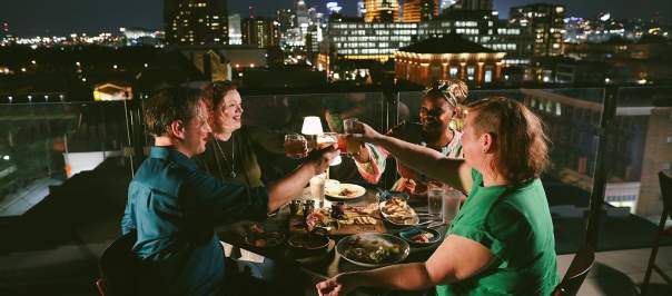 Four people toast each other at night with the Cincinnati skyline in the background