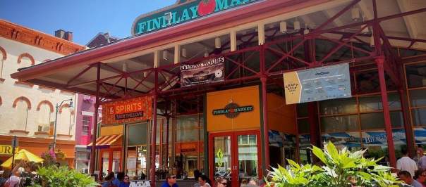The entrance of Findlay Market during the day with couples sitting at tables surrounded by flowers.