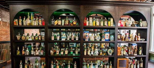 A large 4 row shelf holds vintage spirits