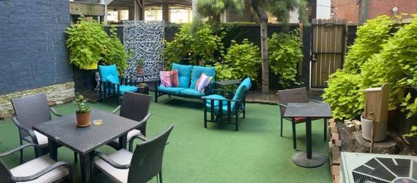 A private patio with several seating options. Green plants grow lush along the wall.