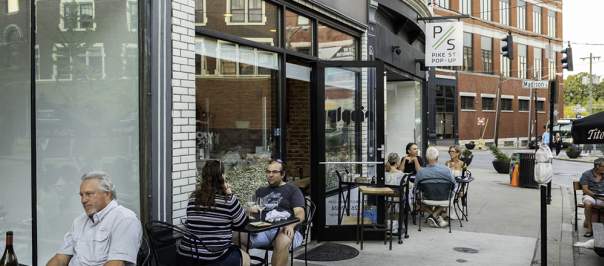 A group of people sits at black metal patio tables on a sidewalk outside Ripple Wine Bar