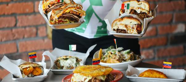 A person offering the viewer tortas in both hands with a table of tortas, empanadas and more food below