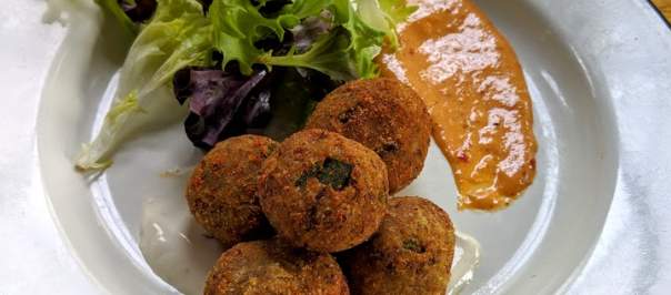 goetta hush puppies from libbys southern comfort in covington ky with green garnish and sauce on the side of a white plate