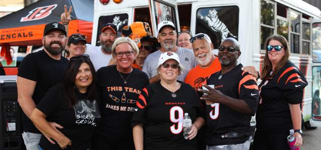 A group of 12 Bengals fans decked out in gear pose in front of a Bengals bus.