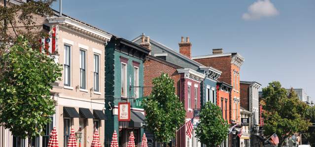 A line of buildings in various colors. There's trees and a grouping of red and white striped umbrellas.