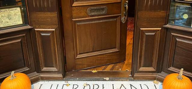 Image is of the bottom of the door and sidewalk up to the door that say's "Hierophany & Hedge" with a pumpkin on each side.