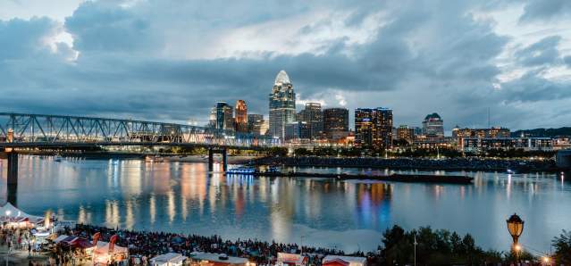 Crowds of people gather along the river as the sun goes down.