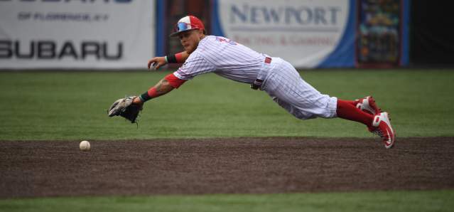 A baseball player is extended midair horizontally to catch a ball.