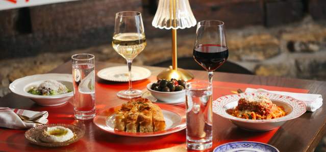 The image is of a table set at Mama's on Main which includes a light, two glasses of wine, two glasses of water, cheese bread, olives, a pasta dish and a salad.
