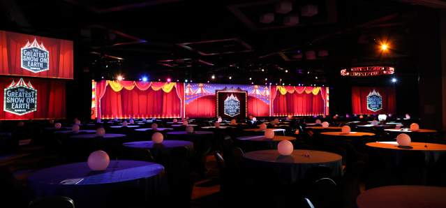Circus signs reading "The Greatest Snow on Earth" hang from red tapestries with many round tables in the foreground