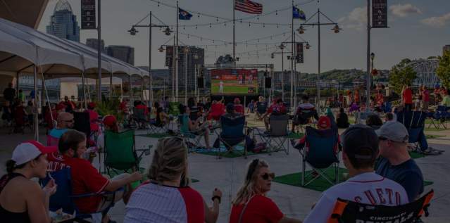 People sitting in lawn chairs wearing Red's gear watching the Red's play on an outside projection screen.