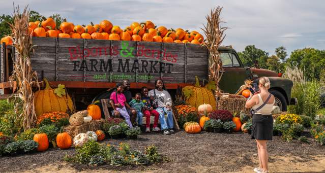 A group poses for a photo in front of a truck full of pumpkins at a fall festival