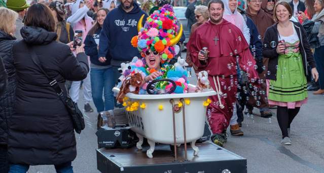 A woman sits in a bathtub during the Bockfest parade wearing a colorful pompom hat