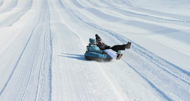 Image is on two people sharing a black inner tube sliding down a hill covered in snow.