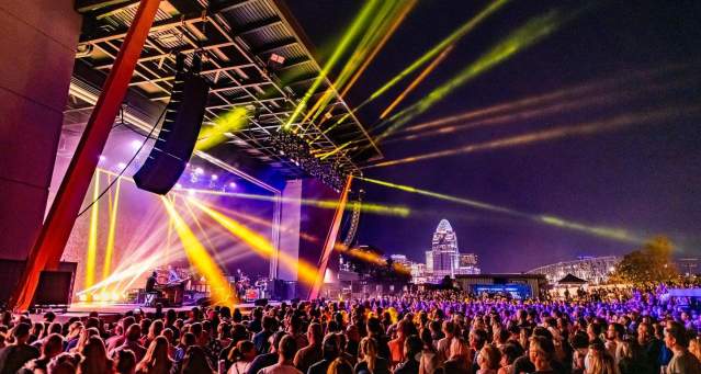 Night concert outdoors with rays of yellow light at Promowest Pavilion in Newport, Ky, with the Cincinnati skyline in the background