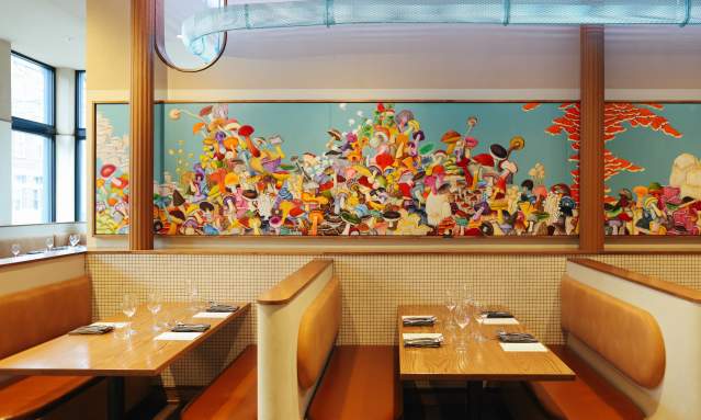 Cozy booths with tables set for dining are in the foreground, while a vibrant, colorful mural fills the background wall.