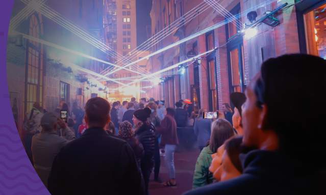 A promotional advertisement for the ArtsWave app features bold white and yellow text in the foreground over a blurred background of a crowded city street at night.