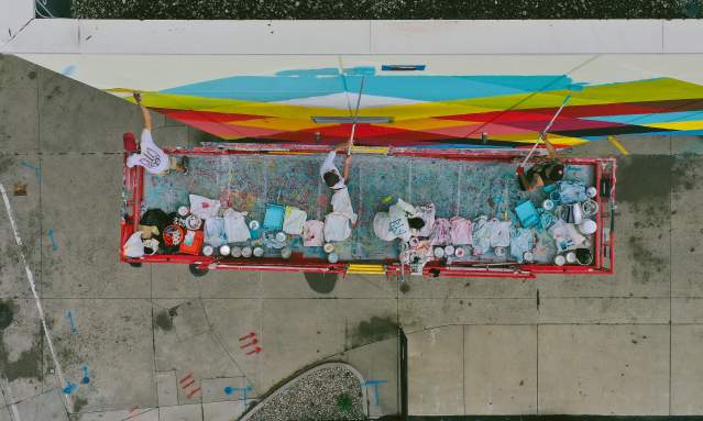 An aerial view of a crew painting a mural on the side of a building