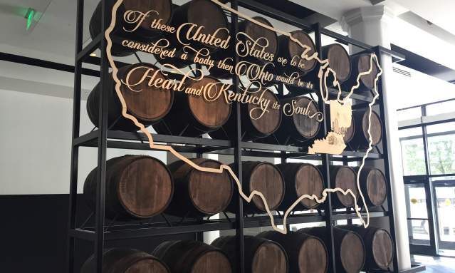 A rack of bourbon barrels with a gold, stenciled map of the U.S.and the words "If the United States are to be considered a body then Ohio would be its heart and Kentucky its soul.