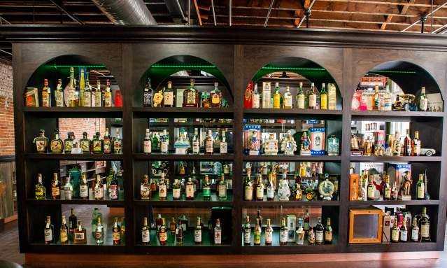 A large 4 row shelf holds vintage spirits