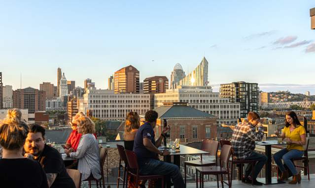 People dining at Opal rooftop restaurant with a view of the Cincinnati skyline in the background