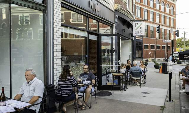 A group of people sits at black metal patio tables on a sidewalk outside Ripple Wine Bar