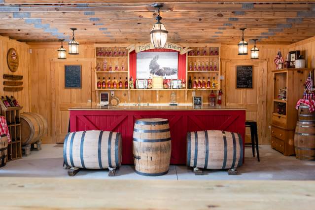 The tasting bar at Becker & Bird Distillery with wooden barrels in front and shelves of bottles lined behind.