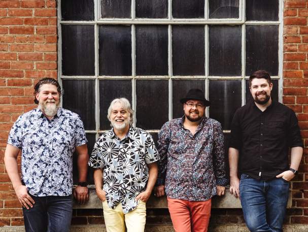 A group of 4 men look into the camera, smiling.