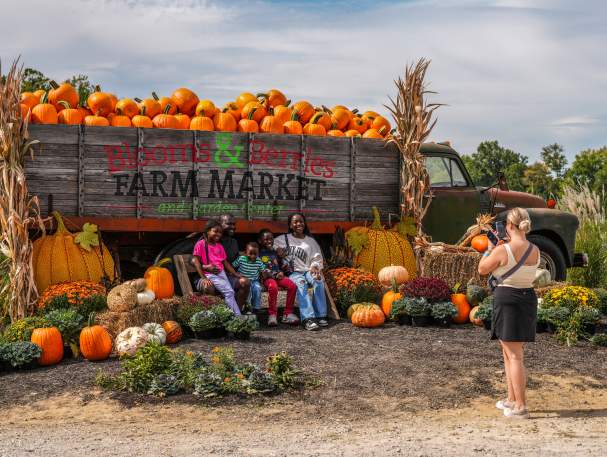 A group poses for a photo in front of a truck full of pumpkins at a fall festival