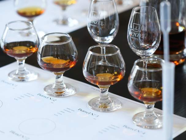 Four bourbon glasses sit on a white placemat next to a small pipette and test tube people can use to make custom blends