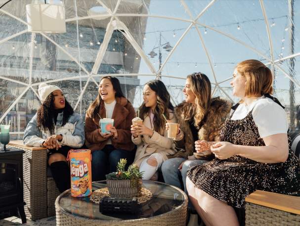 Image is of 5 women sitting in a clear igloo, laughing and having fun.