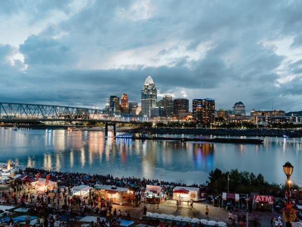 Crowds of people gather along the river as the sun goes down.