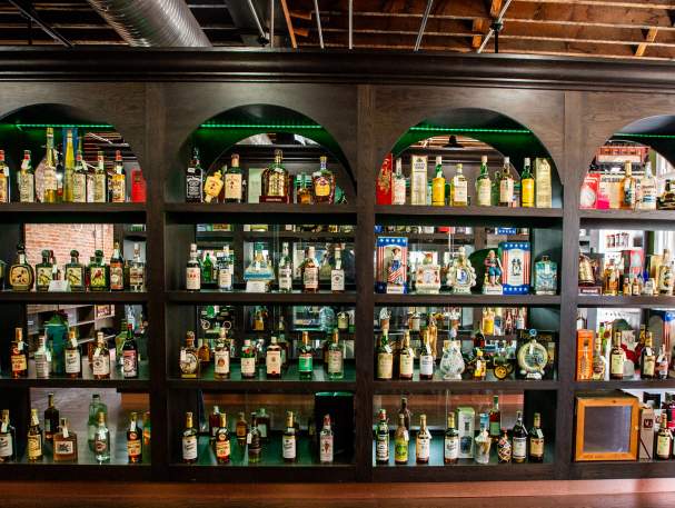 A large 4 row shelf holds vintage spirits