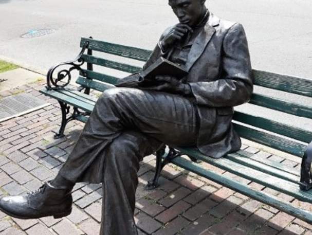 Image is of the bronze statue of James Bradley sitting on a bench, reading a book.