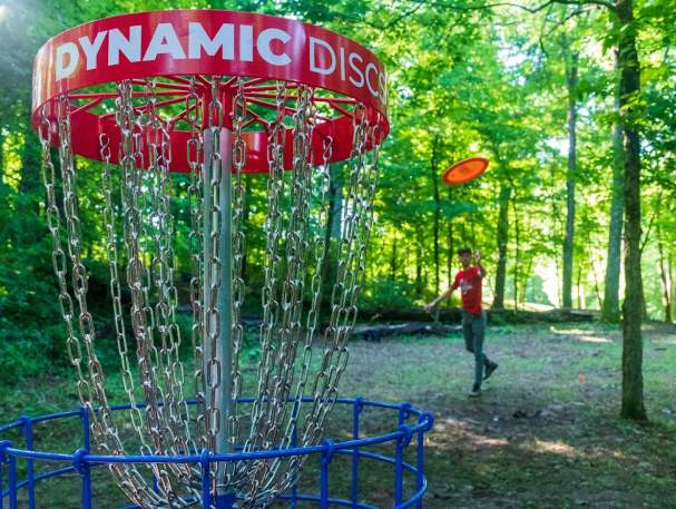 A man throwing a disc to a chain basket at Idlewild Disc Golf course