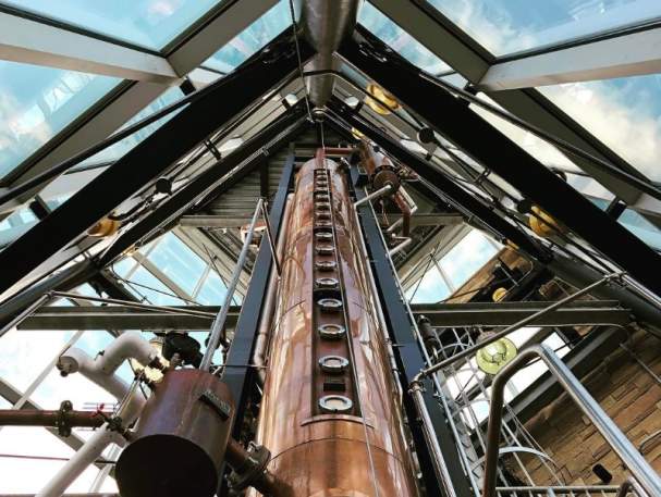 A copper column still that's three stories high, surrounded by clear windows.