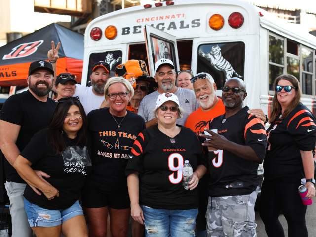 A group of 12 Bengals fans decked out in gear pose in front of a Bengals bus.
