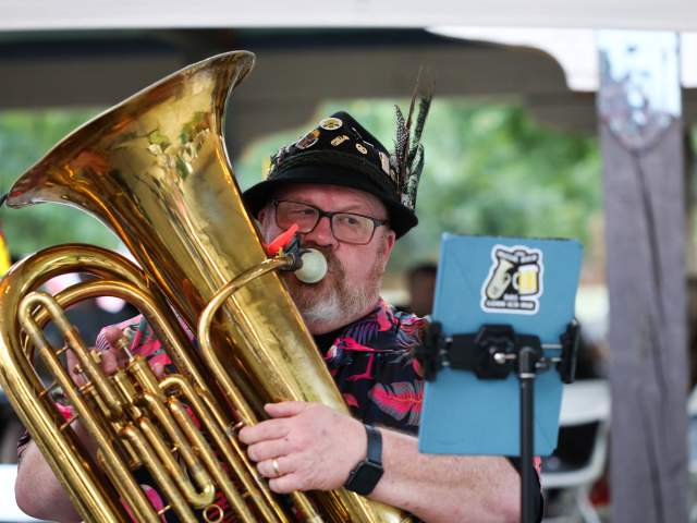 A man plays a tuba while dressed in traditional German clothing.