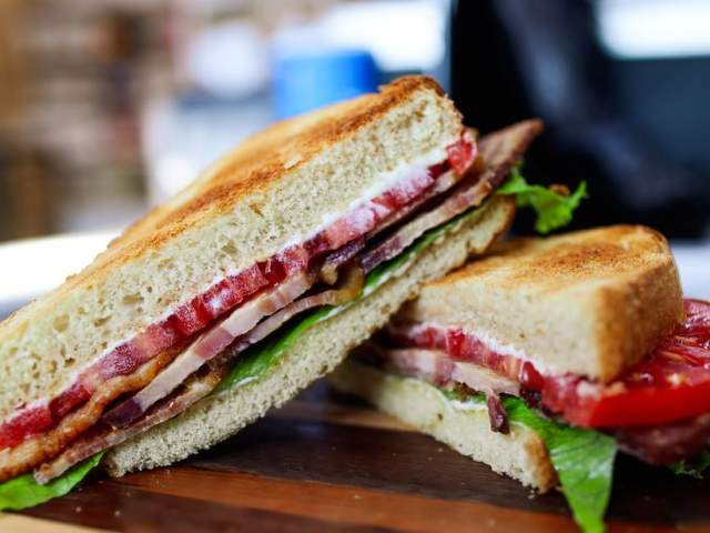 A BLT sandwich cross section with toasted bread, on a wooden board.