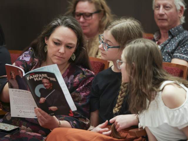 A group of women watching the Cincinnati Symphony Orchestra read through a copy of Fanfare Magazine.