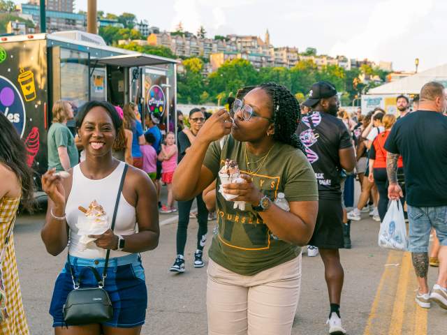 Two women enjoy food at Taste of Cincinnati, with Mt. Adams in the background.