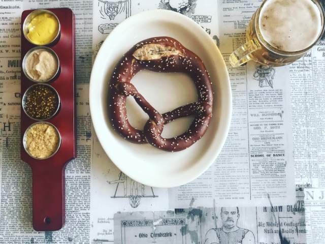 A fresh pretzel, dipping sauces and beer sit on newspaper used as a place mat.
