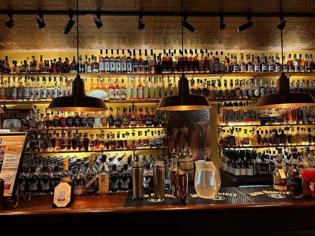 A backlit bar full of different bottles of bourbon
