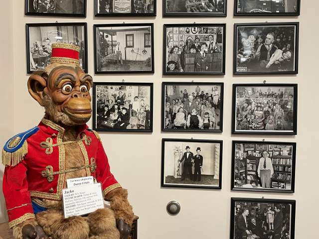 A monkey dummy at Vent Haven Museum is seated in front of a wall of framed historic photographs.