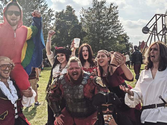 A group of happy people in Renaissance Festival-themed outfits pose for a group photo