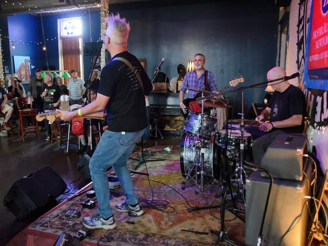 Looking from a stage into the crowd at a music venue. The guitarist/lead singer faces away from the camera.