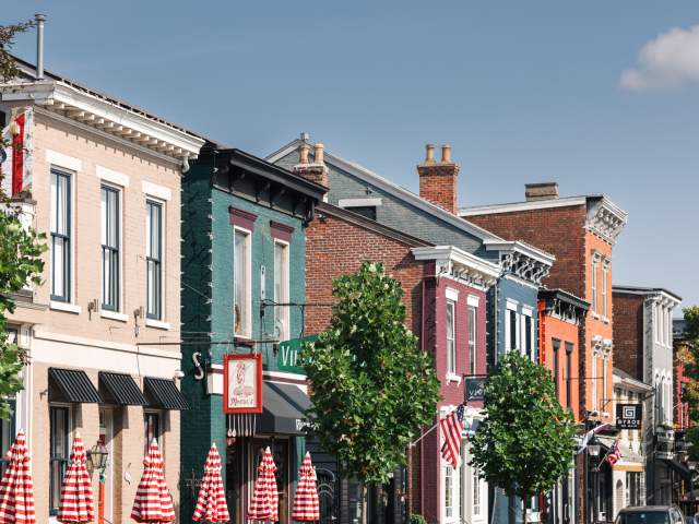 A line of buildings in various colors. There's trees and a grouping of red and white striped umbrellas.